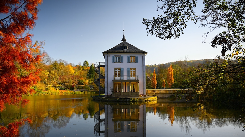 A baroque house, called Trappenseeschlösschen, surrounded by Lake Trappensee in Heilbronn, Germany during autumn. The house and the colorful trees reflect in the water.
