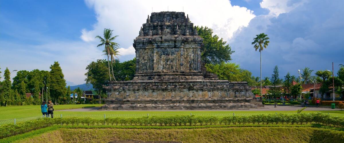 An ancient stone temple with a tiered structure, surrounded by lush greenery and palm trees.