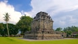 A large stone temple with intricate carvings, surrounded by lush greenery and palm trees.