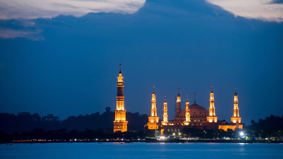 A mosque with multiple minarets and a large dome, illuminated at night.