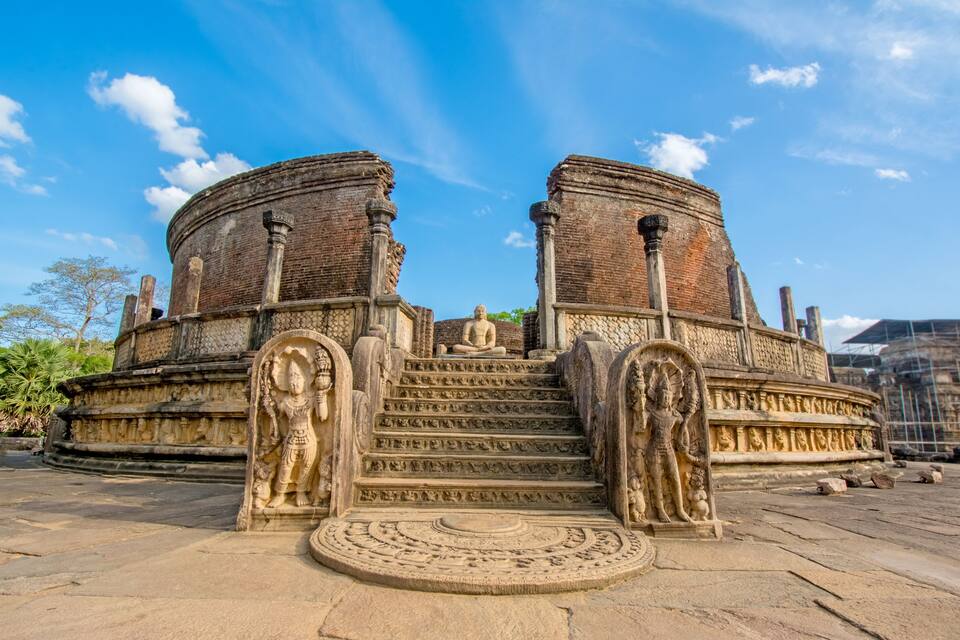 A historical stone structure with a central seated figure, flanked by two large circular towers and intricate carvings.