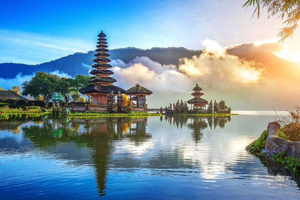 A serene temple complex by a calm lake with a mountain backdrop.