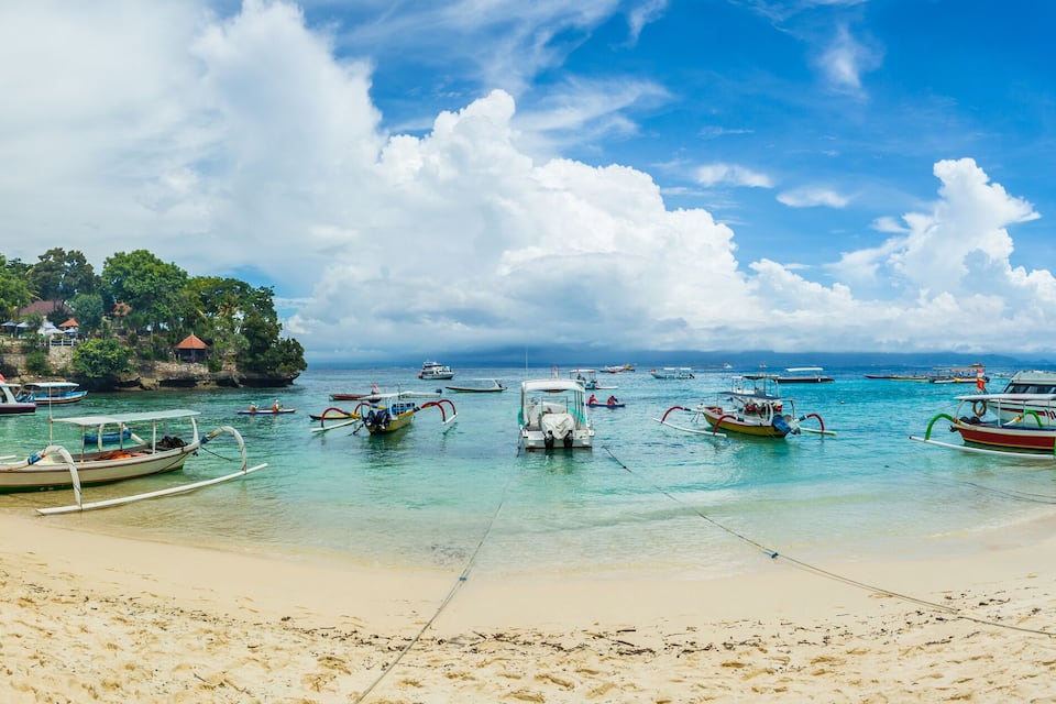 A beach with numerous boats docked and people gathered on the sand.