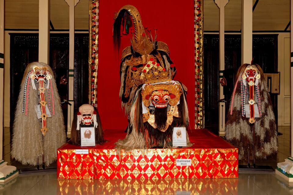 A Balinese mask on a red and gold platform.