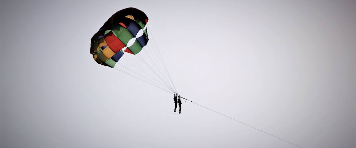 A person skydiving with a colorful parachute against a clear sky.