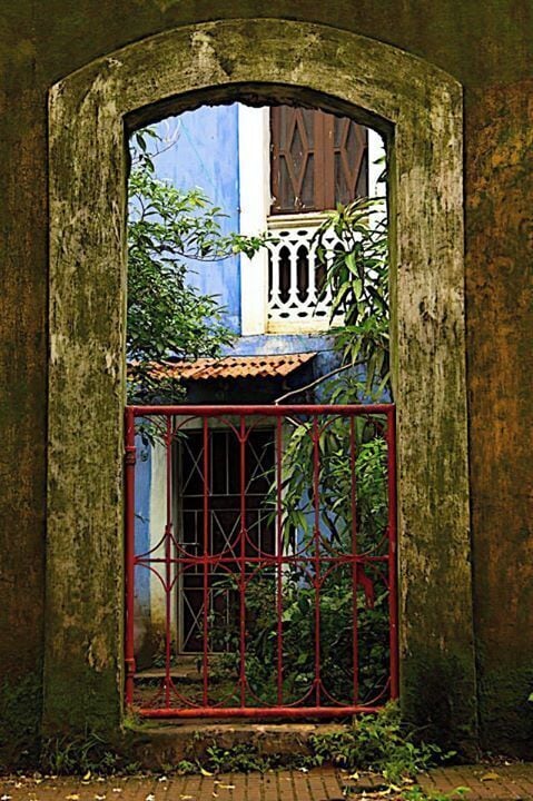 Um arco antigo e desgastado, com uma janela gradeada e vegetação exuberante.