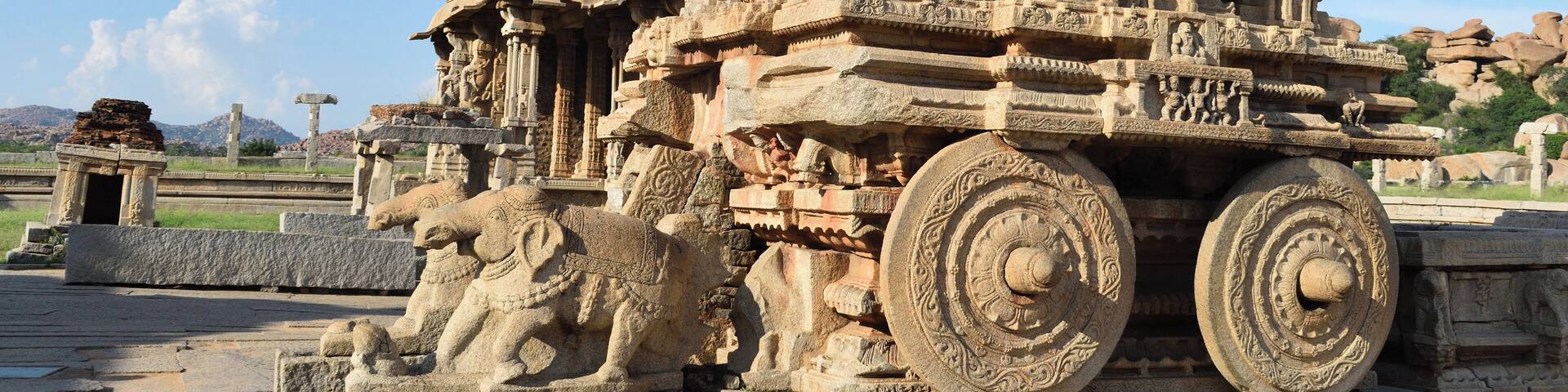 An ancient stone structure with intricate carvings and large wheels.