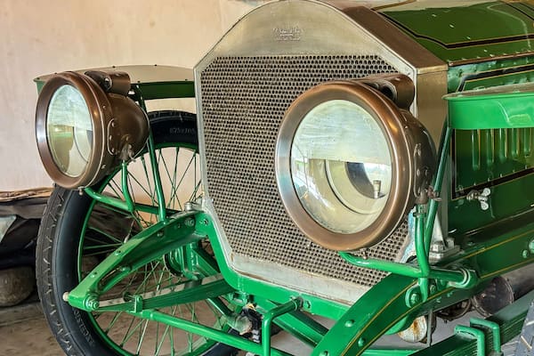 Une voiture ancienne de couleur verte, dotée de grands phares ronds et d’une calandre en treillis métallique.