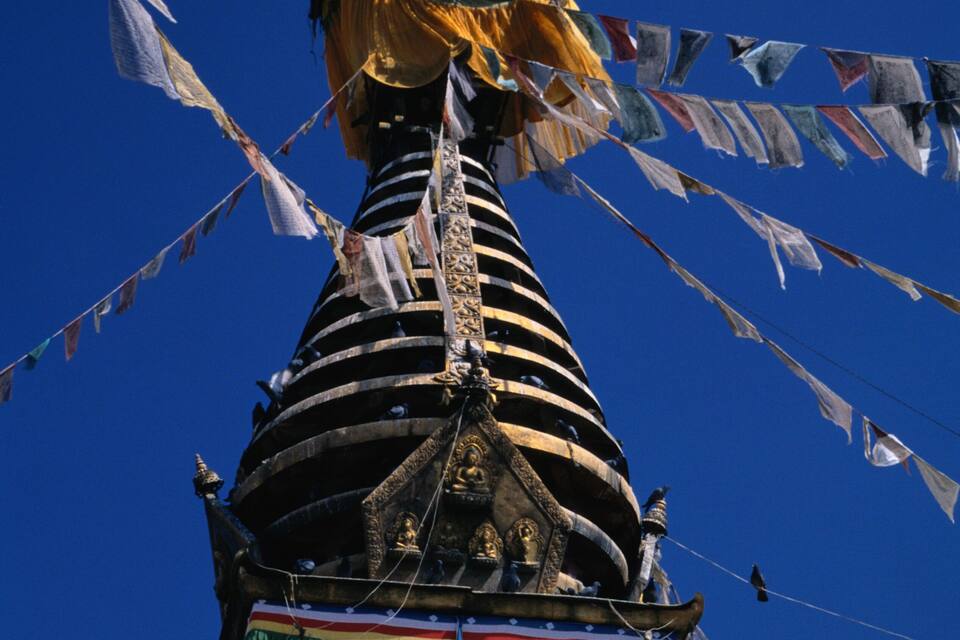A traditional building with a conical roof, colorful prayer flags, and a large eye symbol.