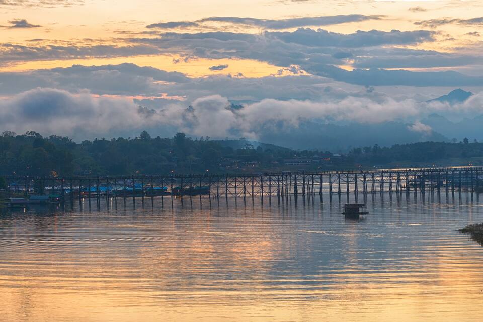 A sunset over a river with a bridge and surrounding hills.