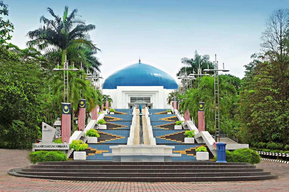 Una imponente escalera conduce a un gran edificio de cúpula azul con banderas de Malasia.