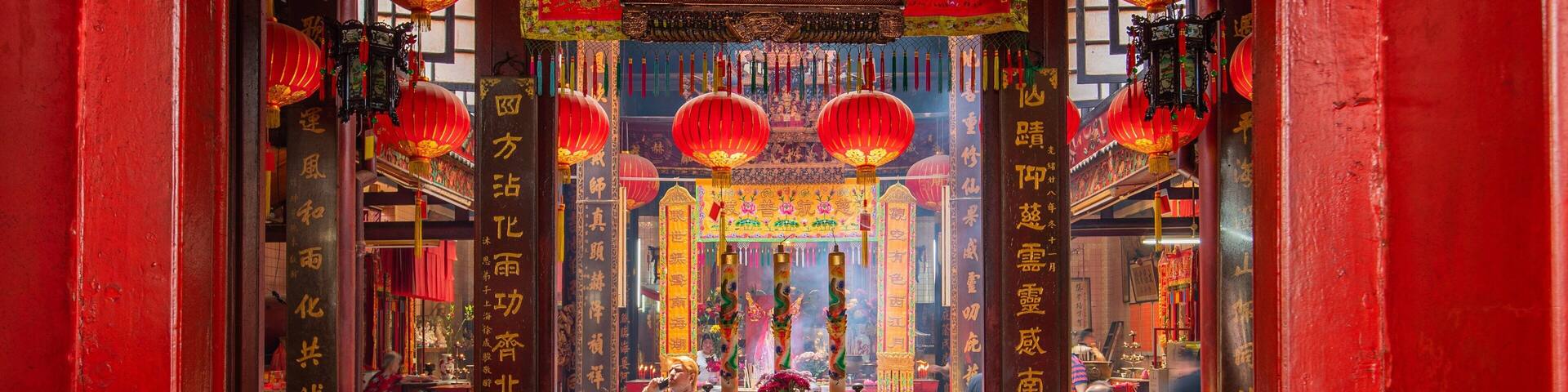 A traditional Chinese temple interior with red lanterns, incense burners, and Chinese calligraphy.