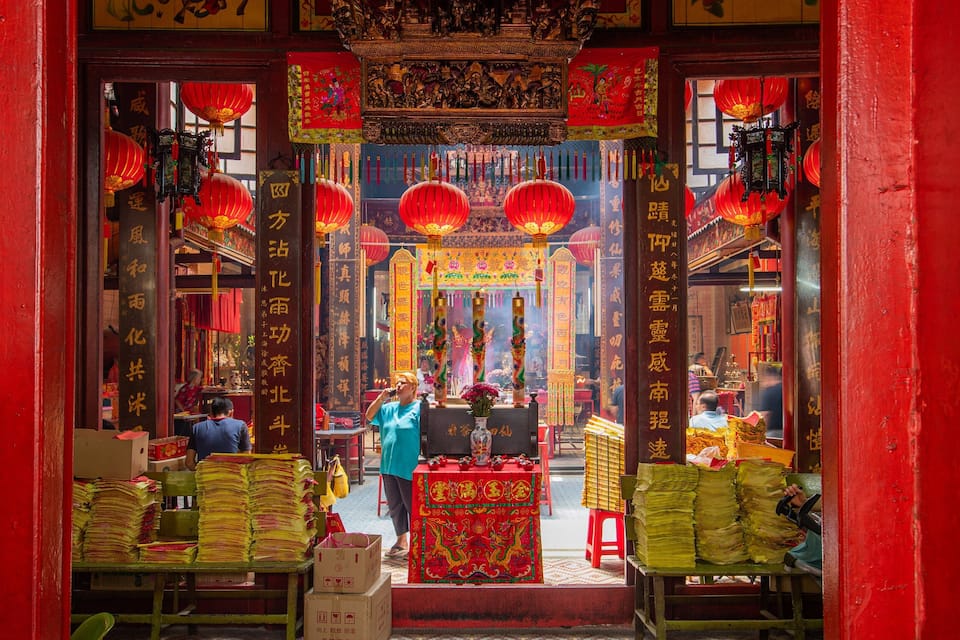 Interior de um templo chinês tradicional, com lanternas vermelhas, queimadores de incenso e caligrafia chinesa.