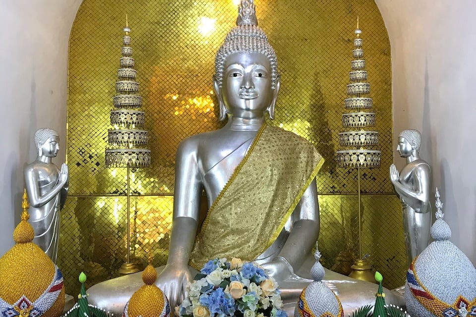 A seated Buddha statue with intricate designs, flanked by smaller statues and decorative elements.
