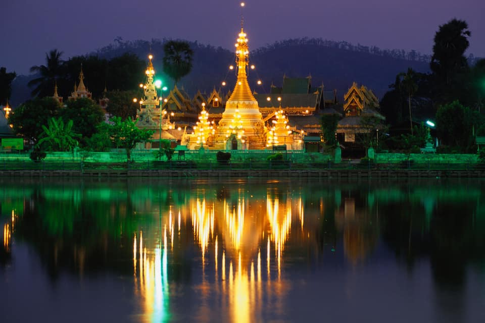 A temple with golden spires reflected in a calm body of water at night.