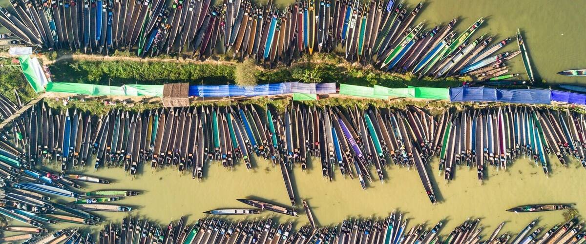 An aerial view of a large number of canoes lined up in rows along a riverbank.