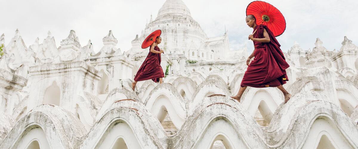 Two novice Buddhist monks with a red umbrellas playing outside the Hsinbyume Temple