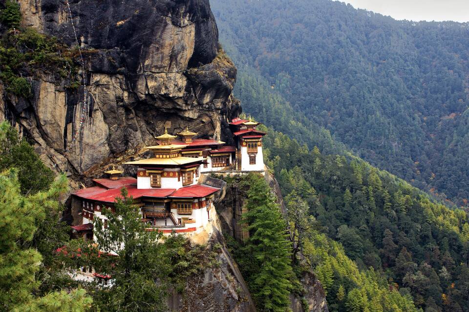 A monastery perched on a cliffside with a forested valley below.