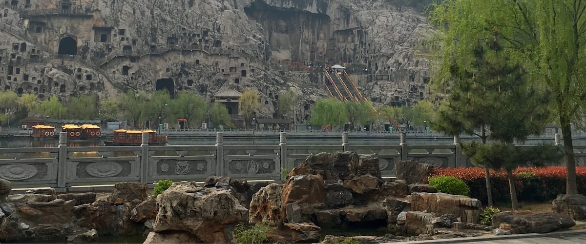 A rocky mountain with ancient rock-cut buildings and a bridge with traditional Chinese architecture.