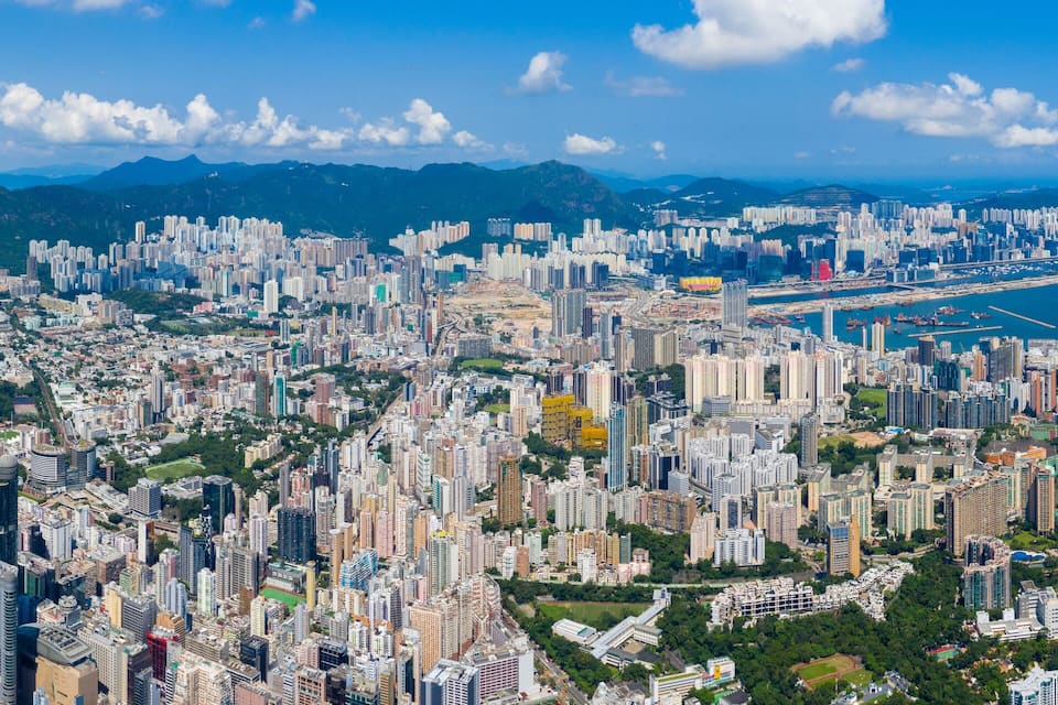 A densely populated city with numerous high-rise buildings, a coastline, and mountains in the background.