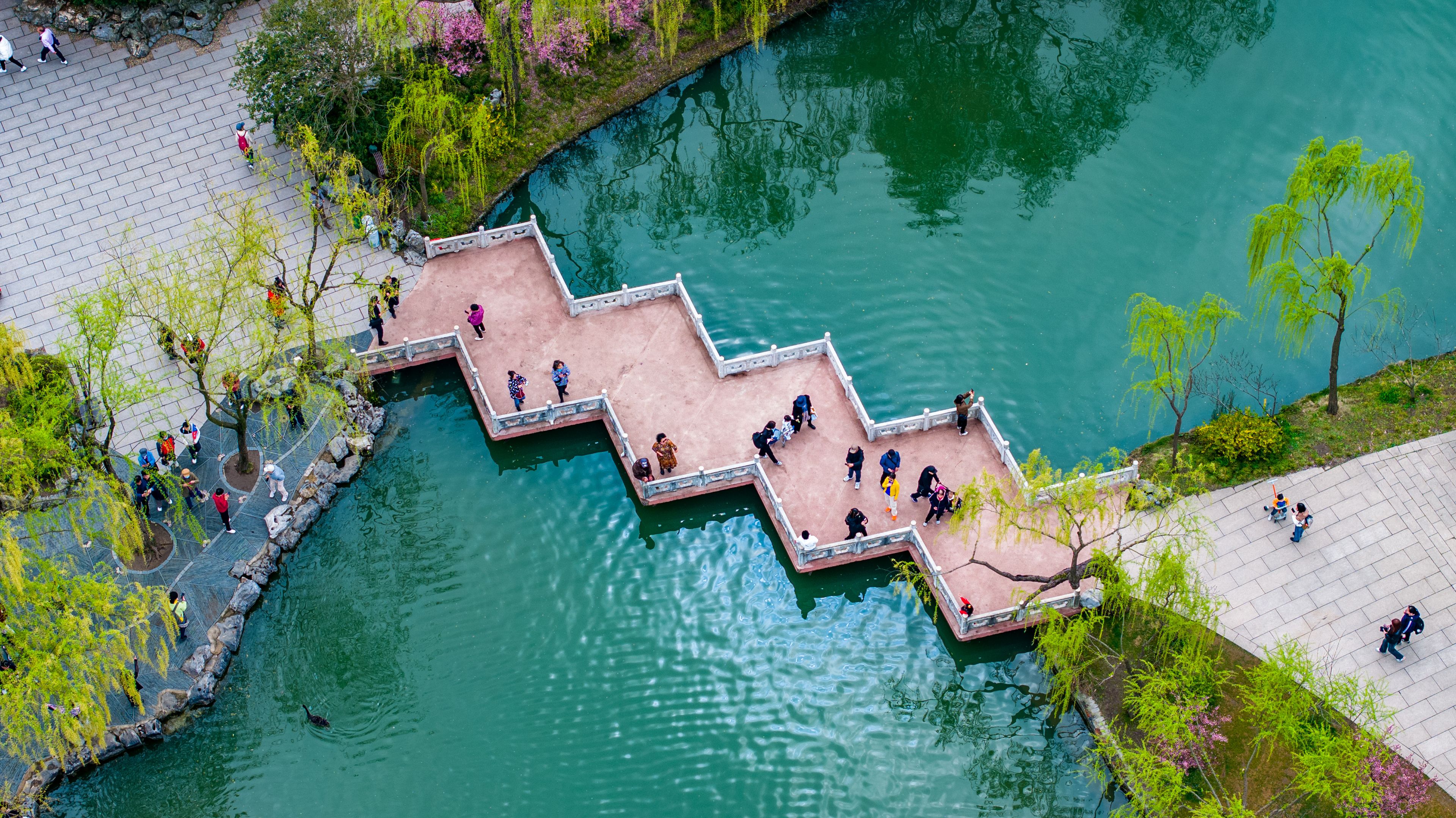 Aerial view of a zigzag stone bridge with visitors walking across green water at Slender West Lake in Yangzhou, Jiangsu Province, China. Scenic Chinese garden landscape with spring atmosphere
