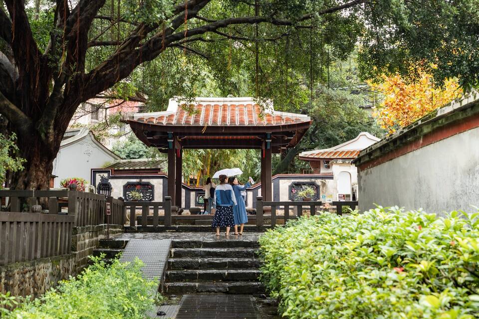 Un jardín japonés tradicional con una escalera de piedra, un pabellón de madera y abundante vegetación.