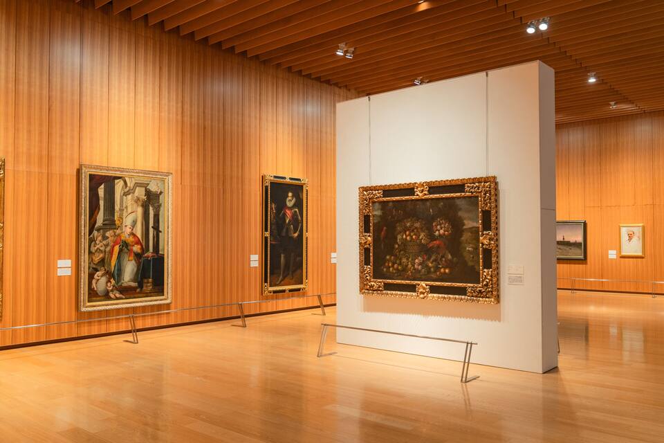 An art gallery with wooden paneling and several framed paintings on display.