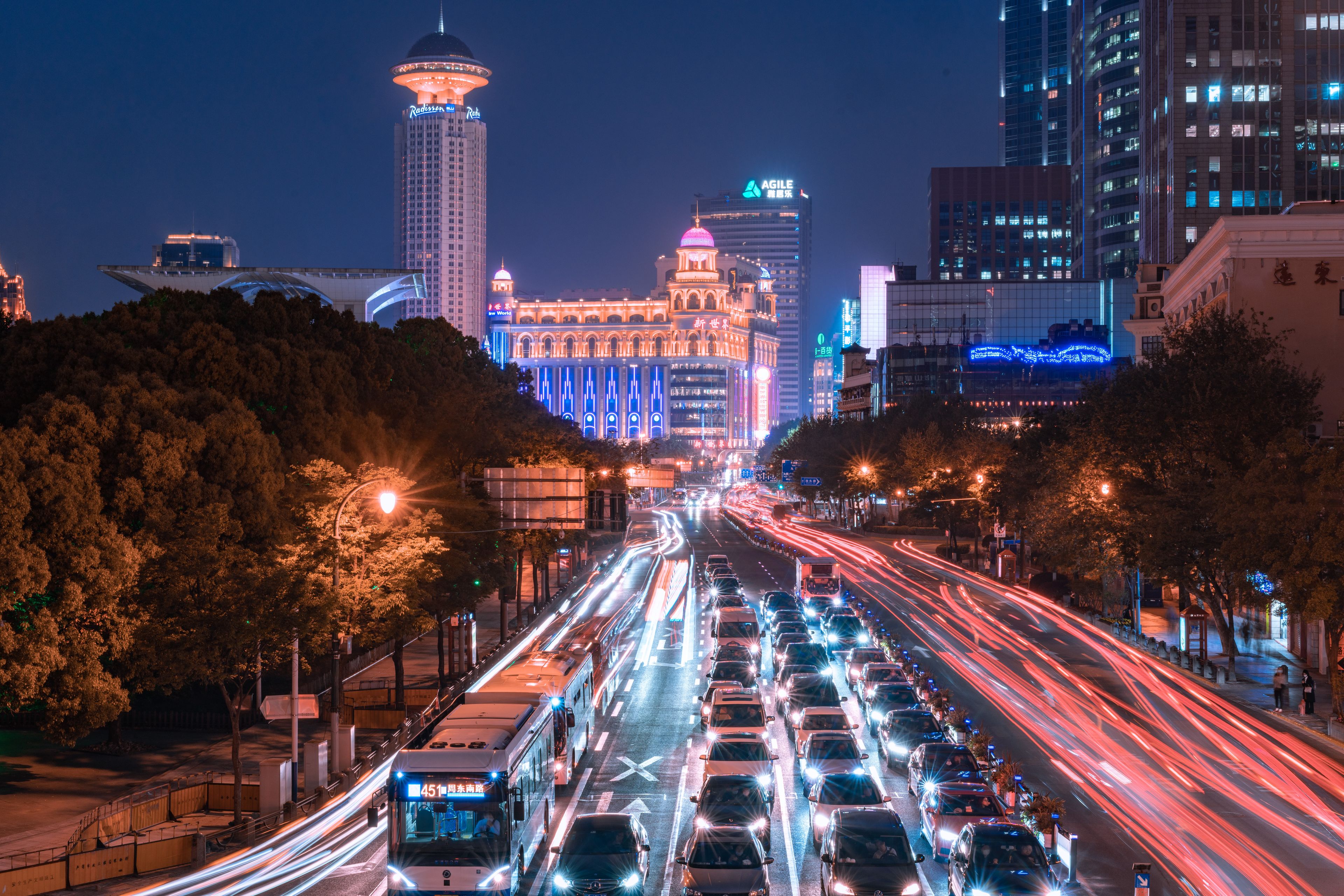 A busy city street at night with illuminated buildings, including a tall tower with a dome and a building with a sign that reads 'New World.'