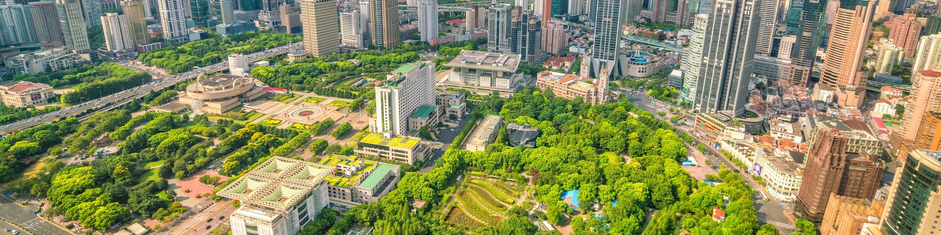 A cityscape with a dense cluster of high-rise buildings, a large green park, and a clear sky with scattered clouds.