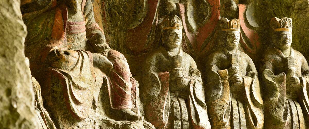 A series of ancient stone statues carved into a cliff face.