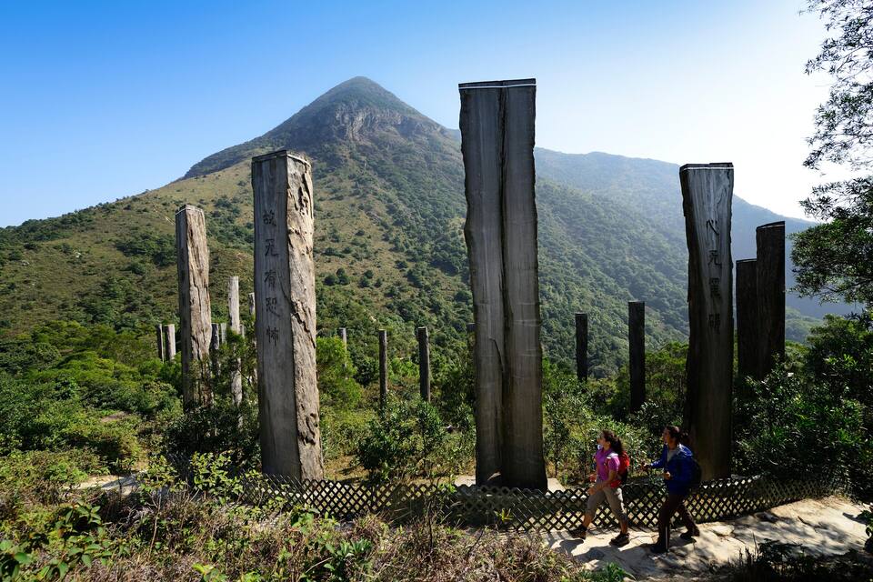 A mountainous landscape with tall, weathered wooden posts and hikers in the foreground.