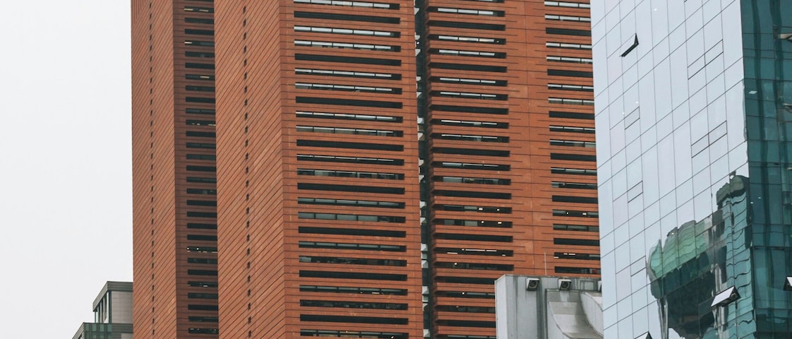 Un edificio alto de ladrillo rojo con el letrero 'KYQBO', rodeado de edificios modernos y tráfico intenso.