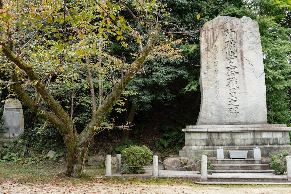 A stone monument with inscriptions, surrounded by trees and a stone pathway.