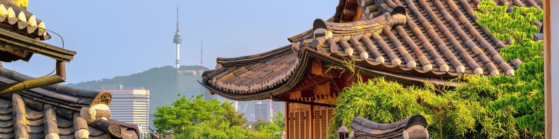 Traditional Korean architecture with tiled roofs and wooden structures, set against a backdrop of modern buildings and a mountain.