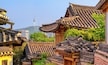 Traditional Korean architecture with tiled roofs and wooden structures, set against a backdrop of modern buildings and a mountain.