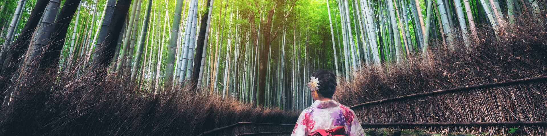 Caminho por uma floresta de bambu com uma mulher e uma criança vestindo trajes tradicionais.