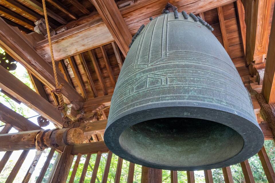 Una campana grande colgada de una estructura de madera, con soga y anillos metálicos a la vista.