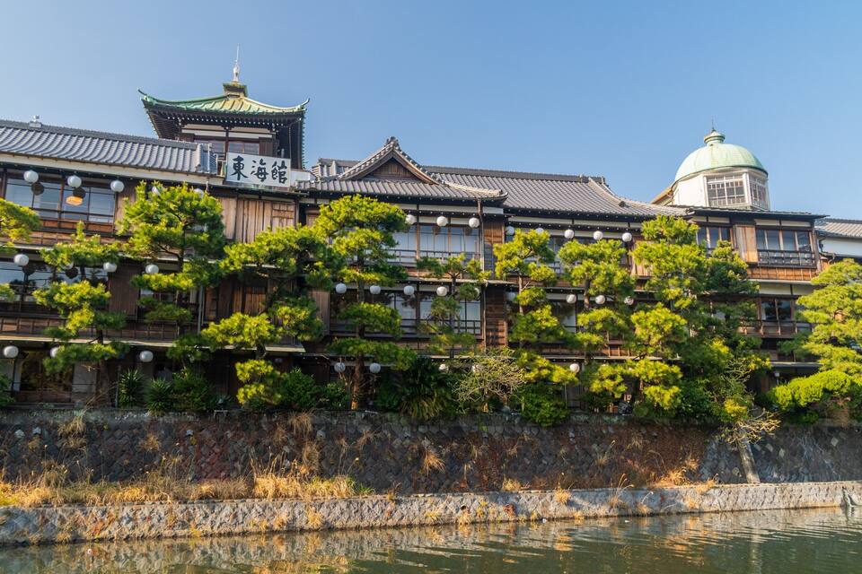 A traditional Japanese building with a pagoda, a large green dome, and a reflection in the water.