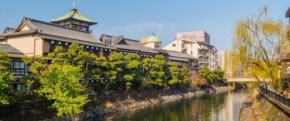 A traditional Japanese town with a river, historic buildings, and a bridge.