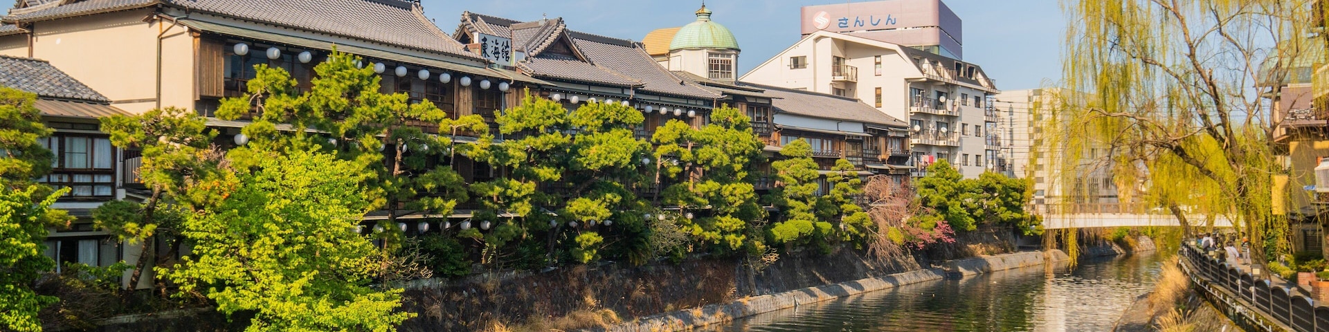 A traditional Japanese town with a river, historic buildings, and a bridge.