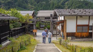 A traditional Japanese village with wooden houses, a stone pathway, and lush greenery.