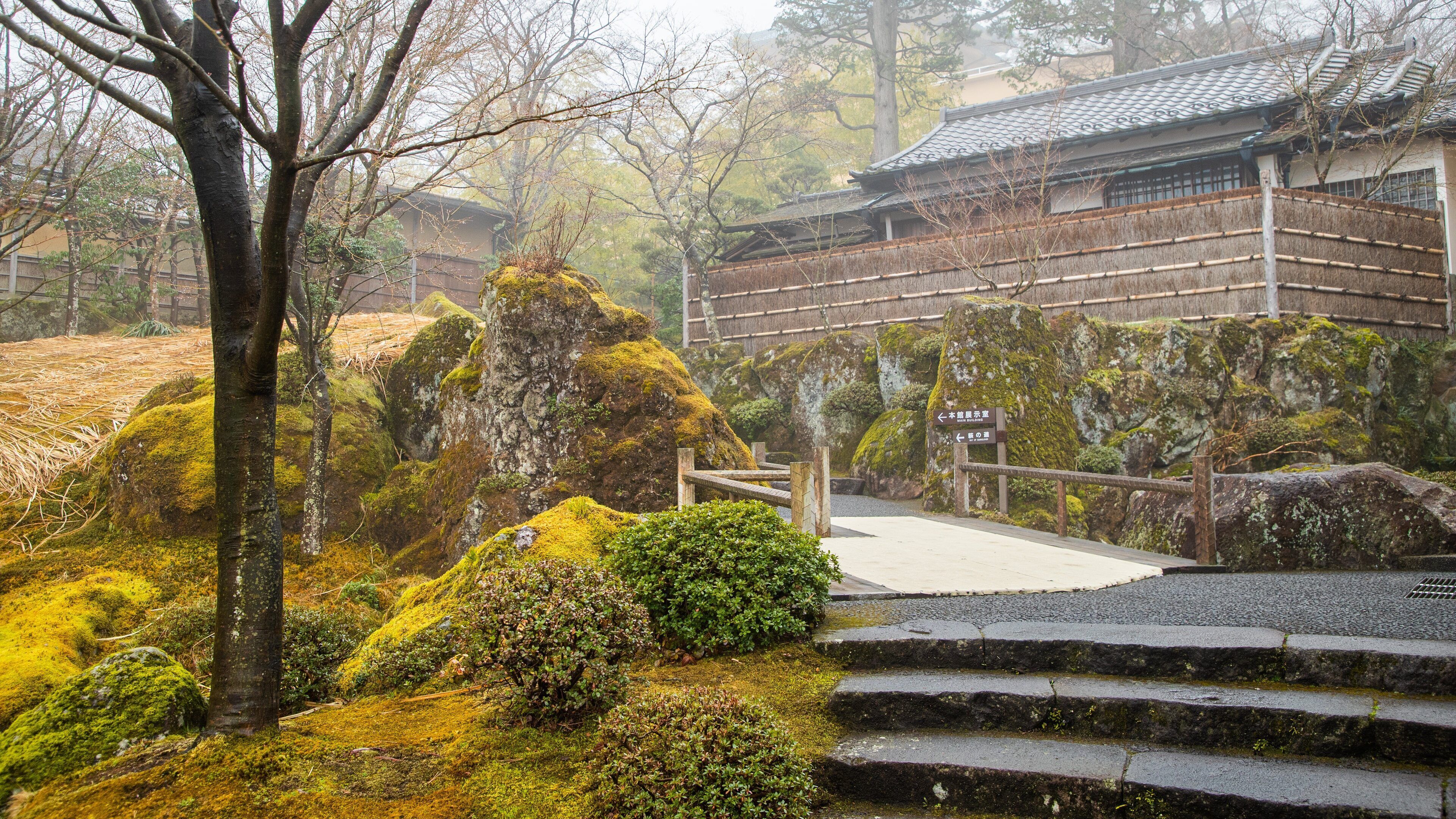 Un edificio japonés tradicional con tejado de cerámica, rodeado de rocas cubiertas de musgo y una escalera de madera que conduce a él.
