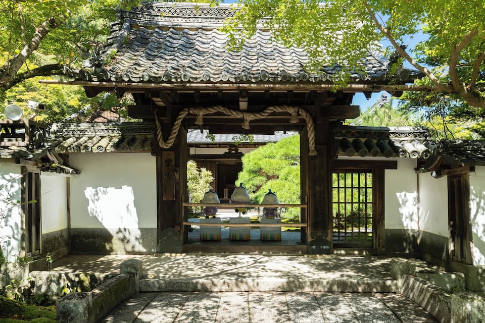 Een traditionele Japanse poort met een pannendak, omringd door stenen trappen en begroeiing.