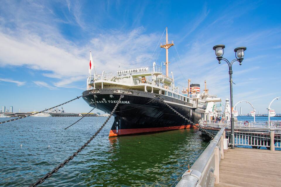 Een groot schip afgemeerd aan een steiger, met een helderblauwe lucht en een stadsachtergrond.