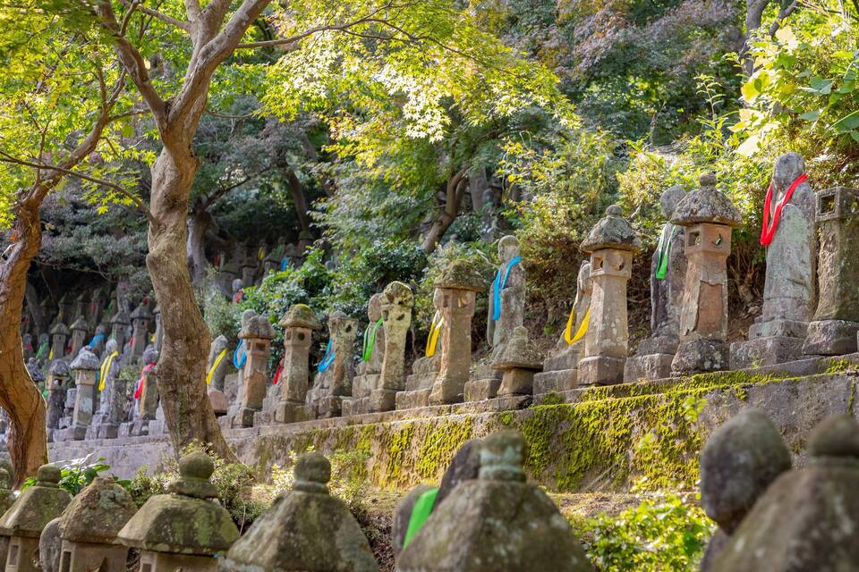 Un sendero de piedra con escalones cubiertos de musgo y faroles de piedra decorados con cintas de colores.