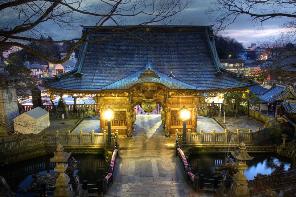 A traditional Japanese temple with a tiled roof, a central courtyard, and a small pond.