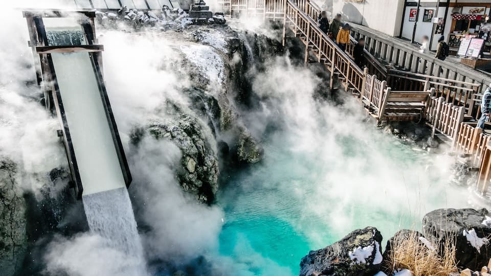 A hot spring with a waterfall, surrounded by rocks and a wooden walkway.