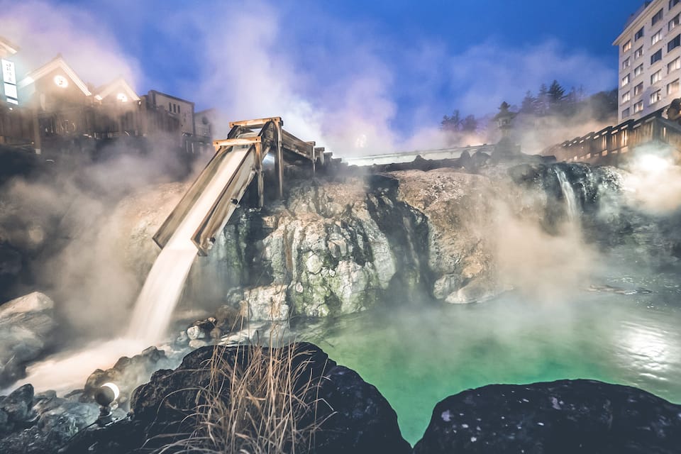 Uma nascente quente com uma passarela de madeira e uma cascata.