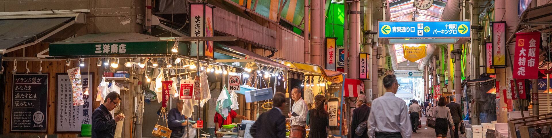 A bustling indoor market with various stalls selling goods, illuminated by hanging lights.