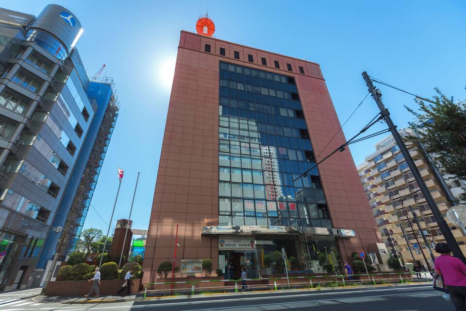 Um edifício alto e vermelho com uma placa azul e branca, rodeado por outros edifícios.